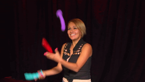 A woman happily juggles three dildos