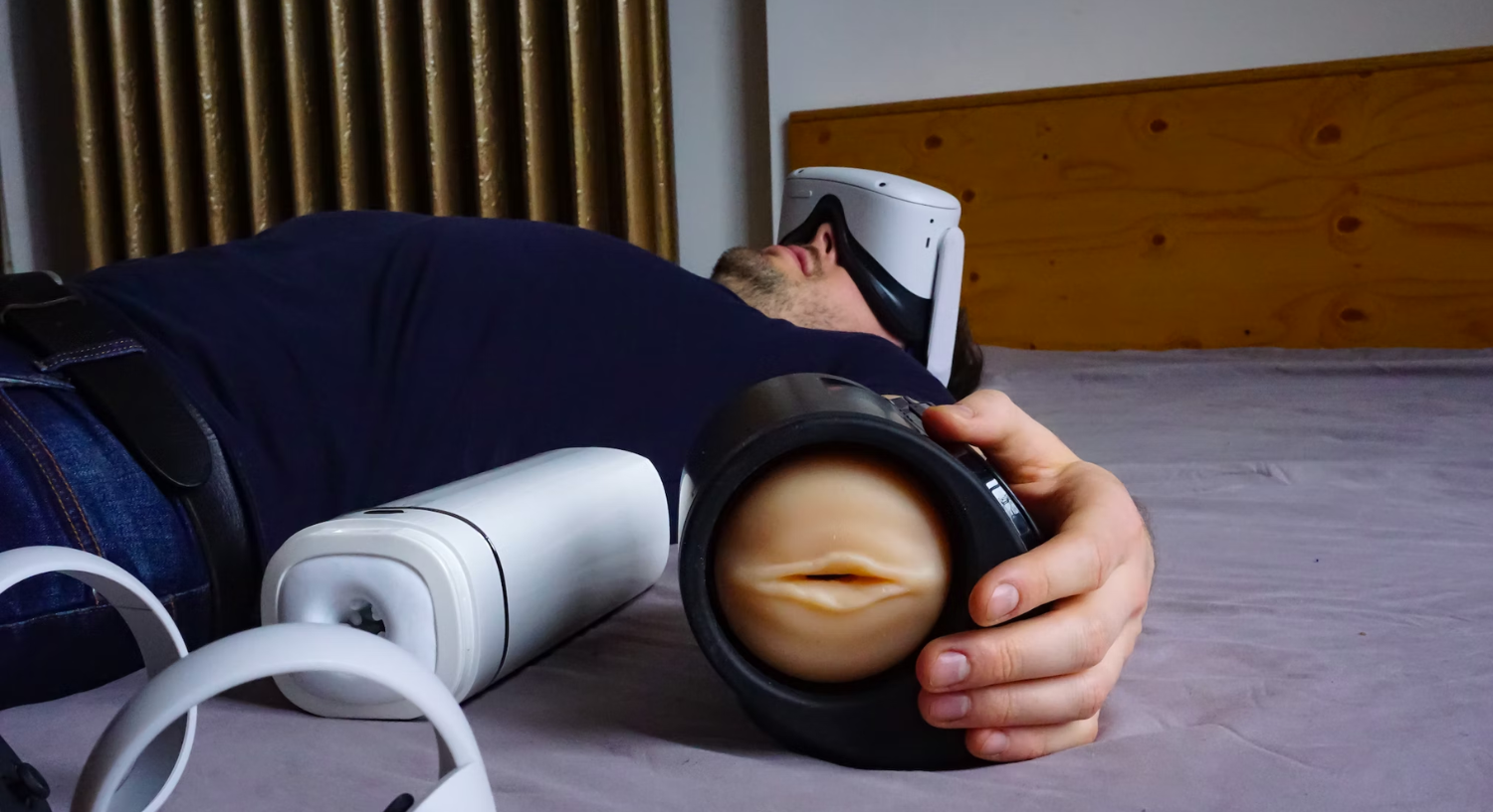 A man lying down wearing a VR headset with an automatic masturbator in his hand