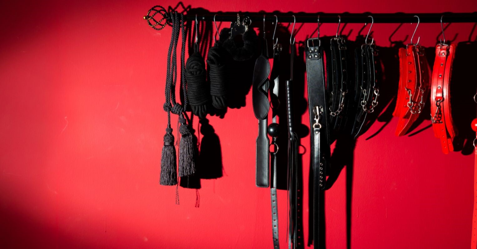 A collection of BDSM toys on a rack against a red wall.