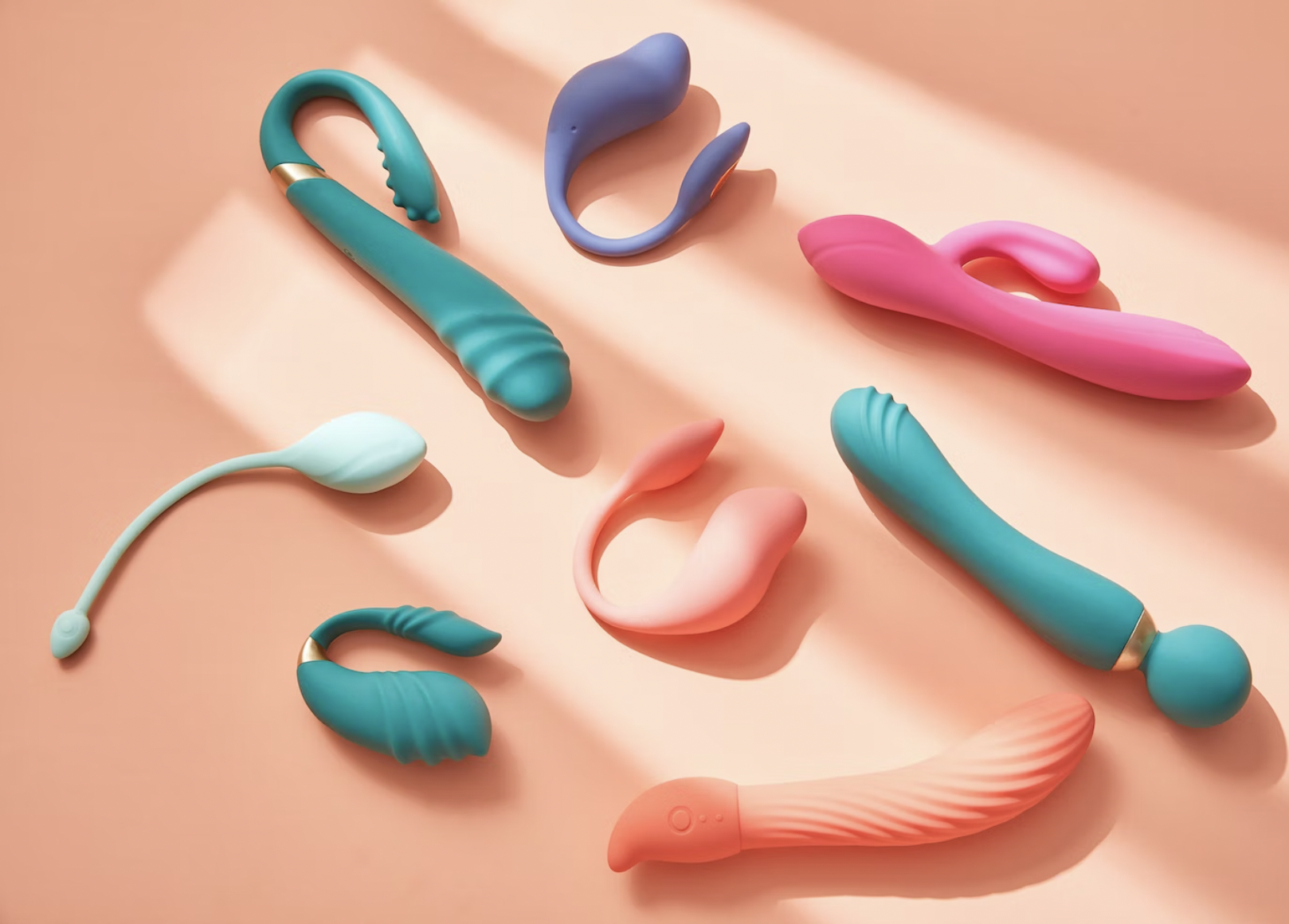 An image of different sex toys for vulva-owners spread across a peach backdrop